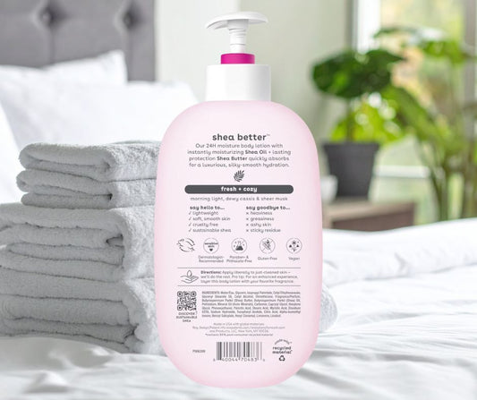 Pink bottle of shea butter product on a bed with gray towels and a blurred room background